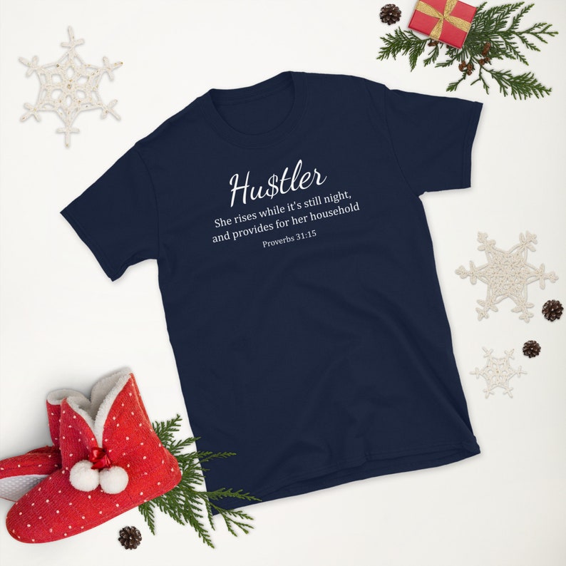 May include: Navy blue t-shirt with white text that reads "Hustler" and a quote from Proverbs 31:15. The quote reads "She rises while it's still night, and provides for her household".