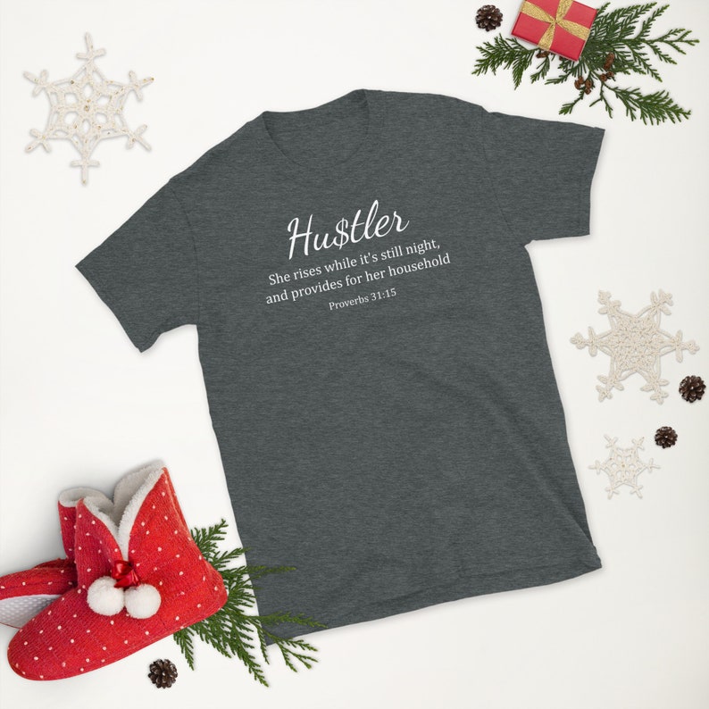 May include: A dark heather grey t-shirt with white text that reads "Hustler She rises while it's still night, and provides for her household Proverbs 31:15".