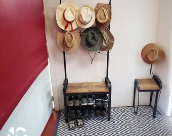 May include: A black metal hat and shoe rack with a wooden seat and shoe storage. The rack holds several straw hats of various styles and colors. A small wooden stool with a hat is to the right. The floor has a black and white geometric rug.