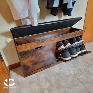 May include: A wooden shoe storage bench with a hinged, padded black top. The bench has a dark brown finish with a drawer and a pull-out shoe rack. Several pairs of shoes are visible on the rack.