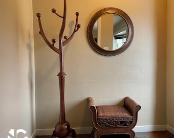 May include: A wooden coat rack with multiple curved arms and ball-shaped knobs. A round, bronze-framed mirror hangs on the wall. A wicker bench with curved arms sits below the mirror. The room has a neutral color palette.