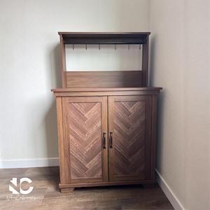 May include: A wooden cabinet with a herringbone pattern on the doors. The cabinet has a top section with hooks and a shelf. The cabinet is brown and has a traditional design. The cabinet is suitable for storage.