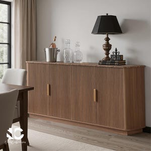 May include: A wooden sideboard with vertical grooved detailing and gold-toned handles. It features a black lamp, decorative bottles, and a wine bucket. The room has a neutral color palette with a window and curtains.