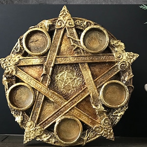 May include: Gold-toned metal pentagram with five circular indentations, each with a raised rim. The pentagram has intricate details and a textured surface.