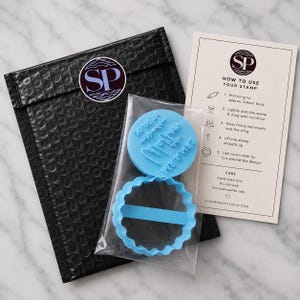 Peut inclure: Un tampon &agrave; gla&ccedil;age bleu clair circulaire avec le texte Mr & Mrs et une date, accompagn&eacute; d'un emporte-pi&egrave;ce festonn&eacute; assorti dans un sachet plastique. Inclut une enveloppe &agrave; bulles noire avec un autocollant SP et une carte d'instructions.