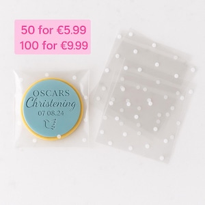 Peut inclure: Un biscuit rond avec un gla&ccedil;age bleu portant le texte OSCARS Christening 07 08 24 et une ic&ocirc;ne de colombe, scell&eacute; dans un sachet en plastique transparent &agrave; pois blancs. Des sachets vides similaires sont empil&eacute;s sur la droite.