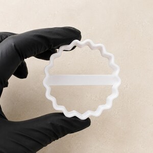 Peut inclure: Un emporte-pi&egrave;ce circulaire blanc avec un bord festonn&eacute; et ondul&eacute;, dot&eacute; d'une barre de support horizontale au centre. L'ustensile pr&eacute;sente un motif dentel&eacute; continu et r&eacute;p&eacute;titif sur tout son p&eacute;rim&egrave;tre ext&eacute;rieur pour d&eacute;couper la p&acirc;te.