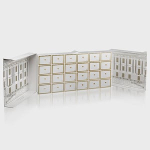 Könnte beinhalten: Ein weißer Adventskalender mit 24 kleinen Schubladen, jede mit einem goldfarbenen Rahmen und einer Nummer. Die Seiten des Kalenders sind mit architektonischen Zeichnungen eines Gebäudes verziert.