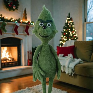 Op de afbeelding: Een handgemaakte groene gehaakte Grinch-pop staat in een gezellige woonkamer. De Grinch heeft grote witte ogen, een ondeugende grijns en is omringd door kerstversieringen, waaronder een boom en een open haard.