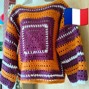 Peut inclure: Un pull crocheté avec des rayures violettes, orange et blanches. Le pull a un motif carré au centre.