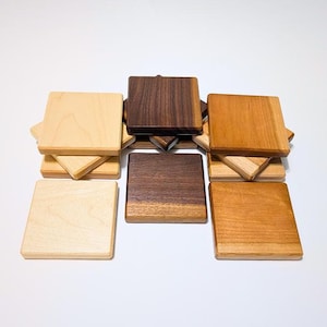 Puede incluir: Colección de posavasos cuadrados de madera en varios tonos de marrón y beige. Los posavasos están apilados y dispuestos, mostrando la veta y las texturas naturales de la madera. Un artículo de decoración para el hogar.