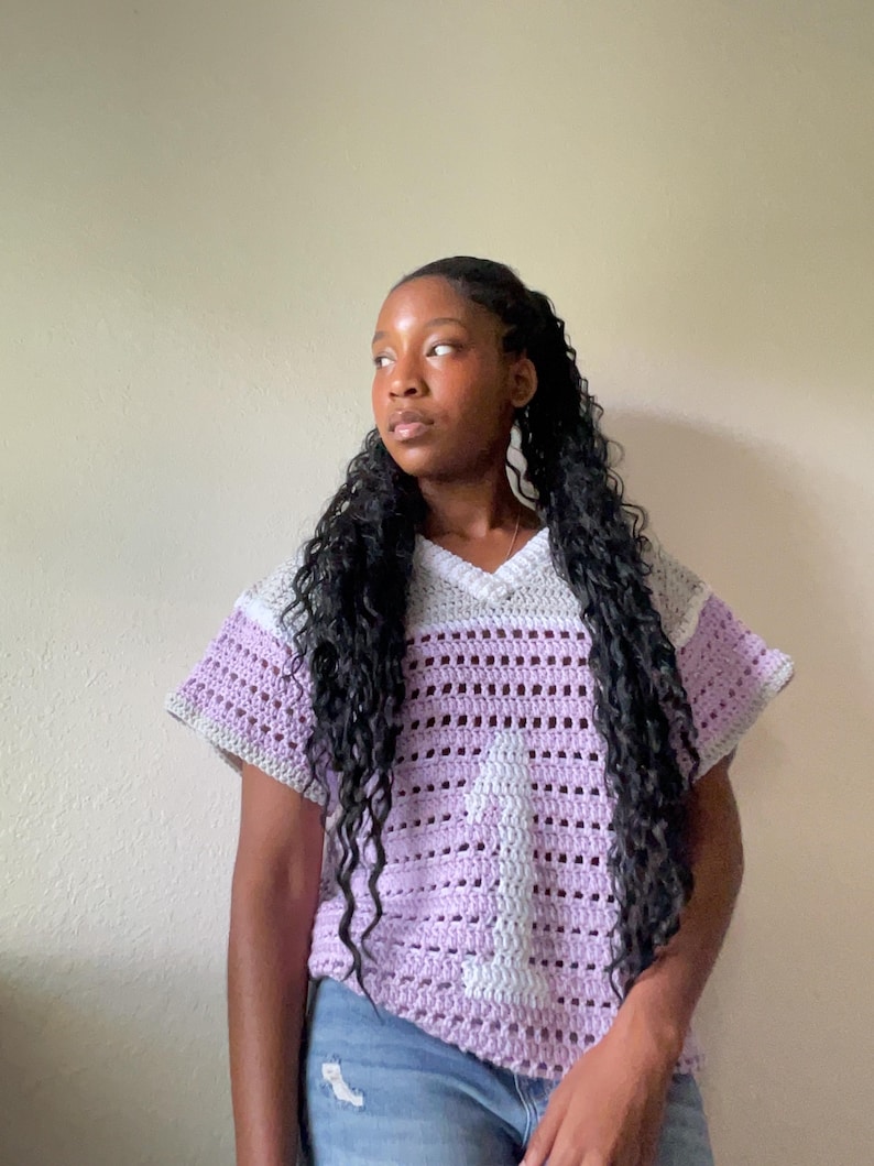 Puede incluir: Una camiseta de crochet de manga corta en lavanda, gris y blanco. La camiseta presenta un cuello en V y un dise&ntilde;o a rayas. El tejido abierto del crochet crea una prenda transpirable y elegante.