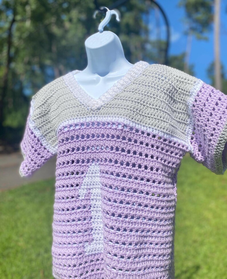Puede incluir: Top de crochet hecho a mano en tonos lavanda, blanco y verde salvia. El top con cuello en V presenta un dise&ntilde;o a rayas con detalles calados. La prenda de manga corta se exhibe en un maniqu&iacute; blanco.