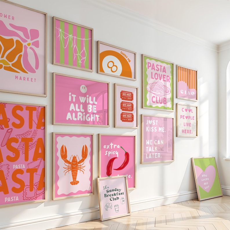 May include: A collection of framed art prints in pink, orange, and green. The prints feature various designs, including text, food illustrations, and abstract shapes. The phrases include "Pasta Lover Club", "It Will All Be Alright", and "Just Kiss Me."