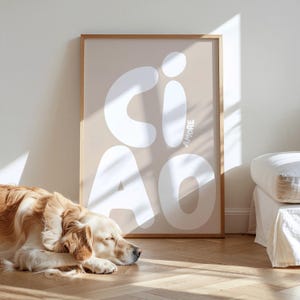 K&ouml;nnte beinhalten: Ein gerahmter Kunstdruck mit dem Wort "CIAO AMORE" in gro&szlig;en wei&szlig;en Buchstaben auf beigem Hintergrund. Ein Golden Retriever liegt auf dem Holzboden vor dem Druck. Der Druck befindet sich in einem hellbraunen Holzrahmen.