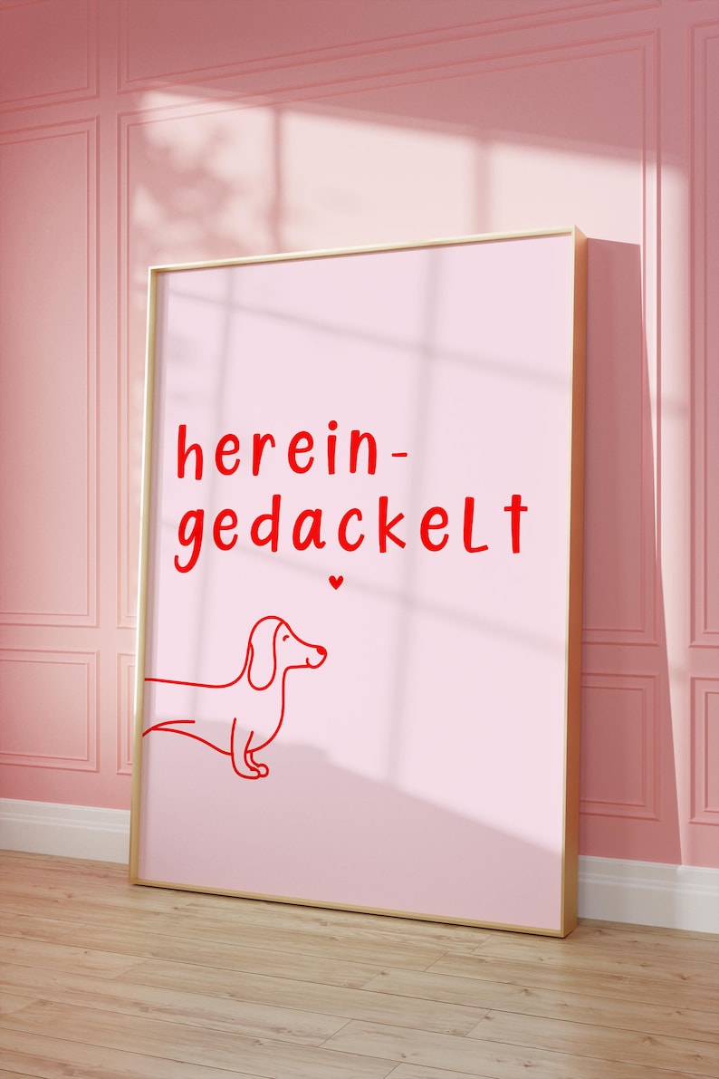 May include: A pink framed poster with the text "herein-gedackelt" in red lettering. A red line drawing of a dachshund is below the text.