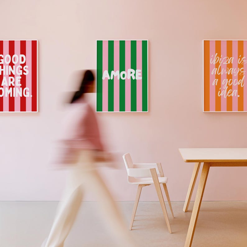 May include: Three framed art prints with text on a pink wall. One print has red and pink stripes with the words "GOOD THINGS ARE COMING." Another has green and pink stripes with the word "AMORE." The third has orange and pink stripes with the words "ibiza is always a good idea."