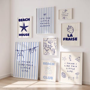 Könnte beinhalten: Eine Sammlung gerahmter Kunstdrucke mit Strandmotiven. Die Drucke zeigen blau-weiße Streifen, Seesterne, Muscheln und Sätze wie "Beach House" und "I think I like this little life." Die Farbpalette ist hauptsächlich blau und cremefarben.
