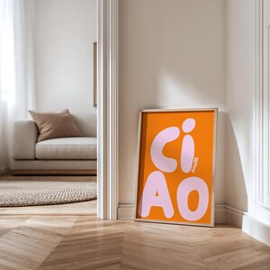 Op de afbeelding: Een ingelijste oranje kunstprint met het woord "CIAO" in grote, roze letters in bubbelstijl. Het woord "AMORE" is verticaal in roze geschreven. De print leunt tegen een witte muur.