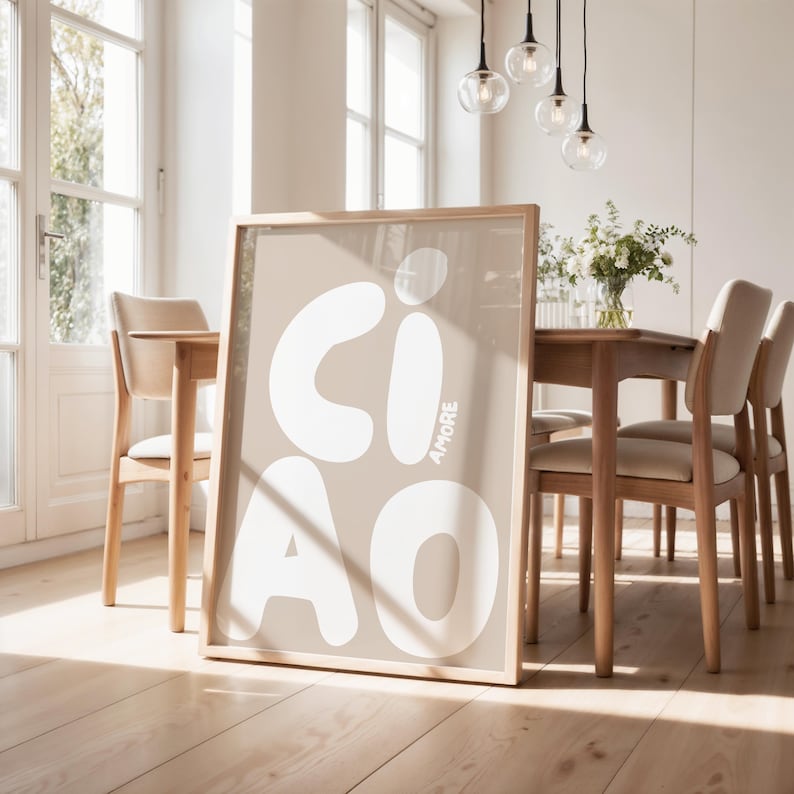 K&ouml;nnte beinhalten: A framed poster with the word "CIAO" in large white letters on a beige background. The word "AMORE" is written vertically on the right. The poster leans against a wall in a dining room with wooden furniture.