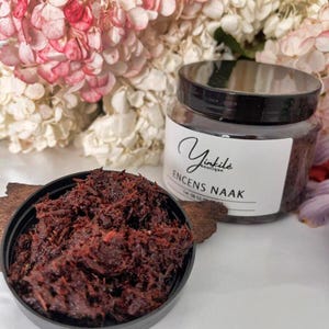 May include: A glass jar of dark brown incense with a white label that reads "Yinkile Boutique" and "Encens Naak". The jar is sitting on a wooden surface with a small amount of loose incense in a black bowl.