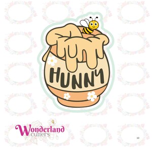 May include: A whimsical cookie cutter in the shape of a honey pot with the word "HUNNY" in bold letters. A cartoon bee sits atop the honey pot. The honey pot is light orange with white daisy accents.