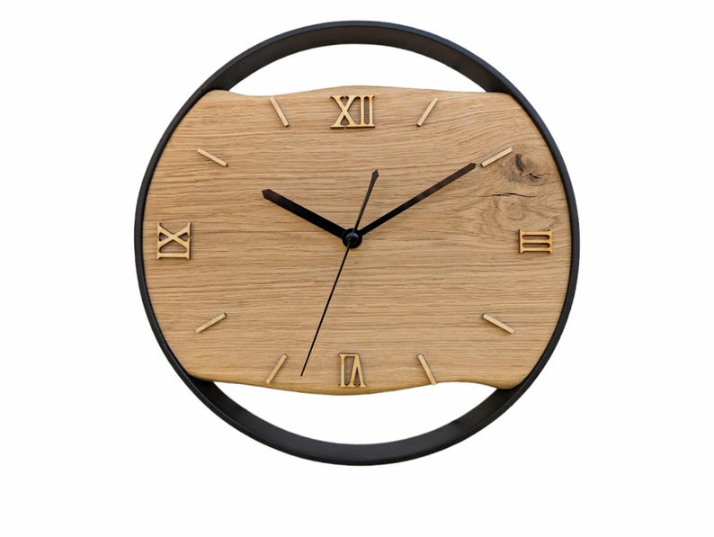 May include: A round wooden wall clock with Roman numeral markings and black hands. The clock face is made of light brown wood with a dark brown wood grain pattern. The clock is surrounded by a black metal frame.