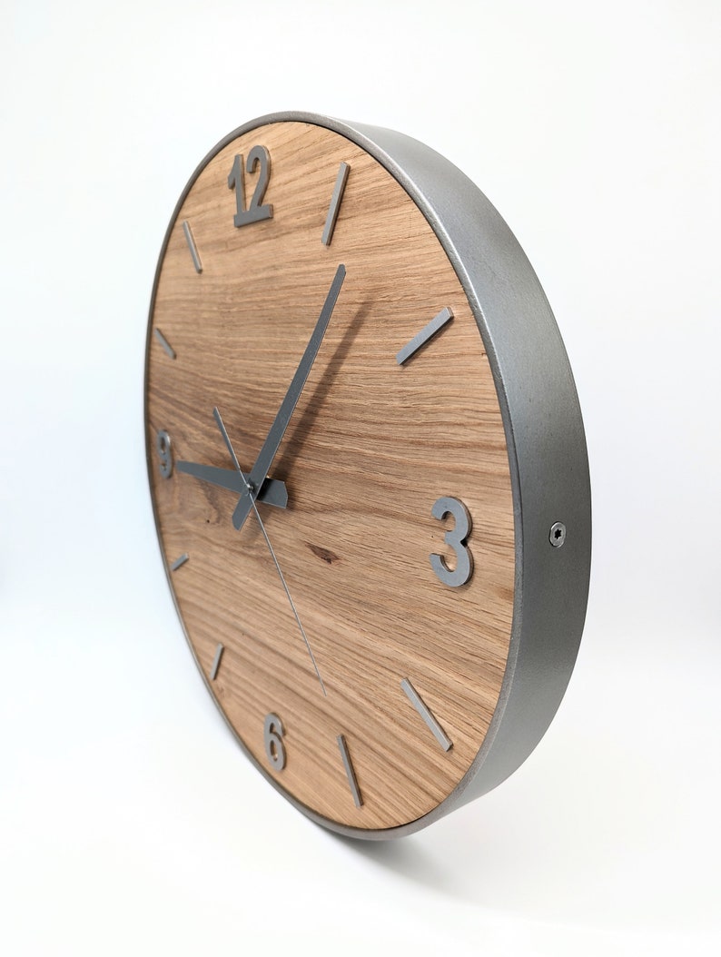 May include: A round wooden clock with a silver metal frame and silver hands. The clock face has Roman numerals for the hours and silver lines for the minutes. The clock is 12 inches in diameter.