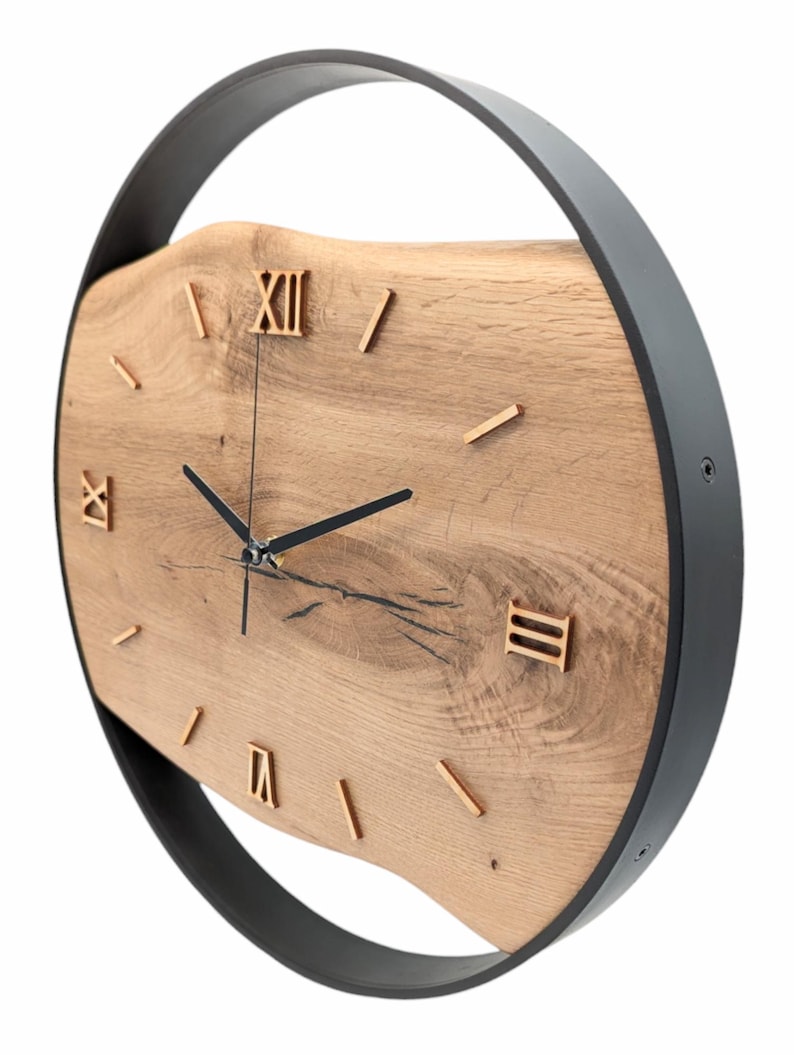 May include: A round, black metal frame surrounds a wooden clock face with Roman numeral markings. The clock face is made of a natural wood slice with a unique grain pattern.