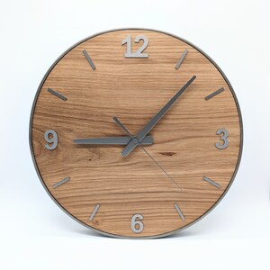 May include: A round wooden clock with silver hands and numbers. The clock face is made of light brown wood with a grain pattern. The numbers 12, 3, 6, and 9 are visible on the clock face.