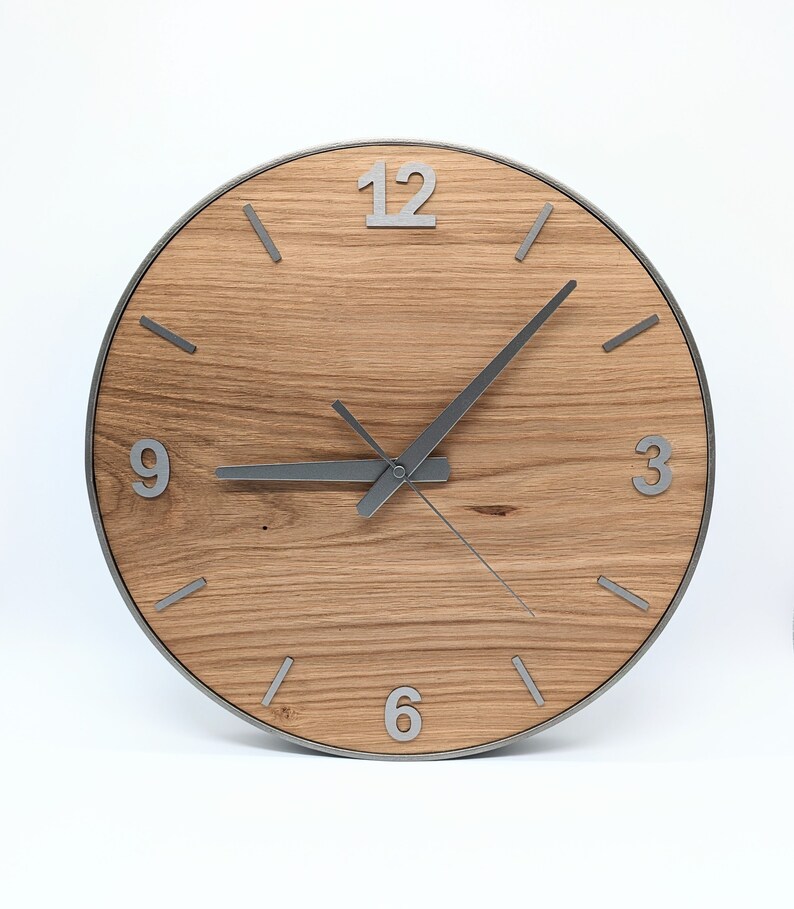 May include: A round wooden clock with silver hands and numbers. The clock face is made of light brown wood with a grain pattern. The numbers 12, 3, 6, and 9 are visible on the clock face.