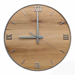 May include: A round wooden clock with Roman numeral markings and silver hands. The clock face is made of light brown wood with a natural grain pattern.