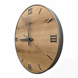 May include: A round wooden clock with Roman numeral markings and black metal hands. The clock face is made of light brown wood with a dark brown wood grain pattern. The clock has a silver metal frame.