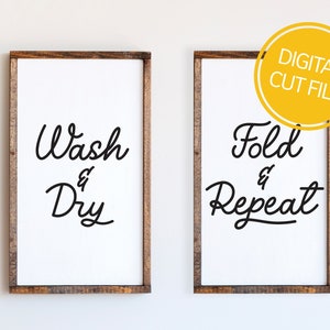 May include: Two framed laundry room signs. The left sign reads "Wash & Dry" in black script on a white background. The right sign reads "Fold & Repeat" in black script on a white background. Both signs have a dark brown wooden frame.