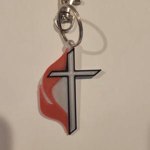 May include: A red and white flame-shaped keychain with a silver cross and a silver split ring.