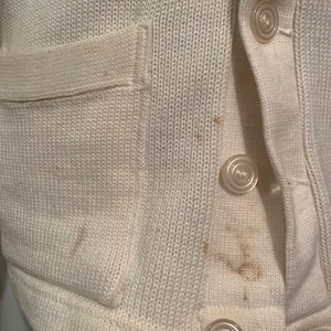 May include: A white knitted cardigan with a patch pocket and button closure. The cardigan has a few brown stains.