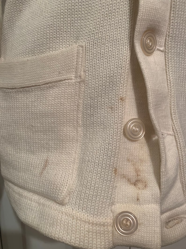 May include: A white knitted cardigan with a patch pocket and button closure. The cardigan has a few brown stains.