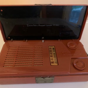 Puede incluir: Radio Emerson vintage en una caja marr&oacute;n con tapa negra. La radio tiene una rejilla de altavoz, dial de sintonizaci&oacute;n y dos perillas de control. El texto "Emerson Radio and Phonograph Corporation NY USA" es visible.