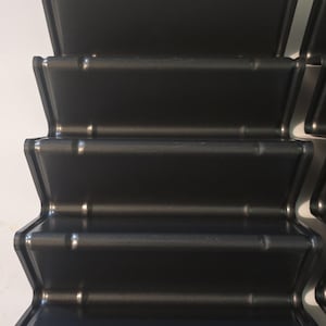 May include: Dark grey, multi-sectioned baking pan. The pan has a unique, accordion-like design with multiple sections. The pan is made of a non-stick material. The image shows the pan from a top-down perspective.