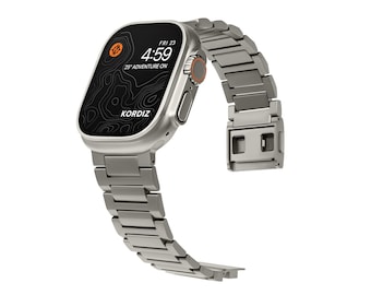 May include: A silver Apple Watch with a black face and a silver metal band. The watch face displays the time, date, and a compass icon. The text on the watch face reads "FRI 23" and "4:59". The text below the time reads "25% ADVENTURE ON". The text at the bottom of the watch face reads "KORDIZ".