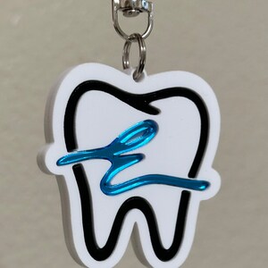 May include: White tooth-shaped keychain with a black outline and a blue swirl design.