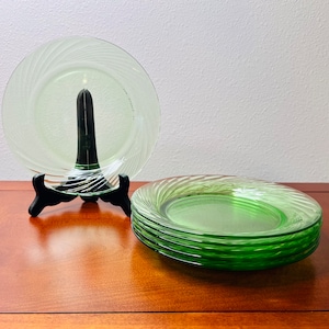 May include: A set of six green glass plates with a swirl design. The plates are stacked on top of each other and are sitting on a wooden table.
