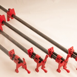 May include: Four red pipe clamps with black metal bars. The clamps are in different sizes and are arranged in a row from largest to smallest.