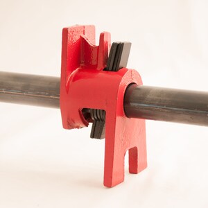 May include: Red metal pipe clamp with black rubber pads. The clamp is attached to a black metal pipe.