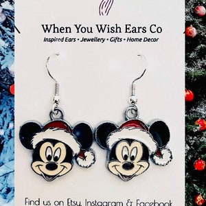 May include: A pair of silver dangle earrings featuring a cartoon Mickey Mouse wearing a Santa hat. The earrings are on a white background with the text "When You Wish Ears Co" and "Inspired Ears - Jewellery - Gifts - Home Decor".