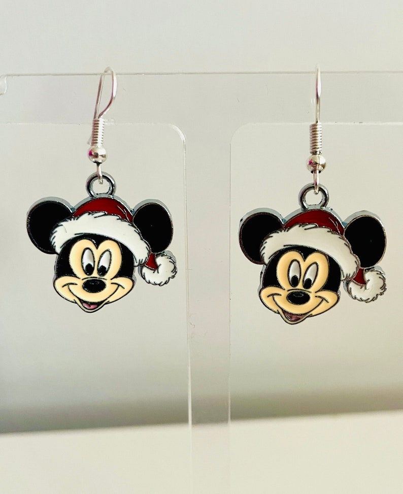 May include: A pair of silver dangle earrings featuring a cartoon image of Mickey Mouse wearing a Santa hat. The earrings are silver with red and white accents.