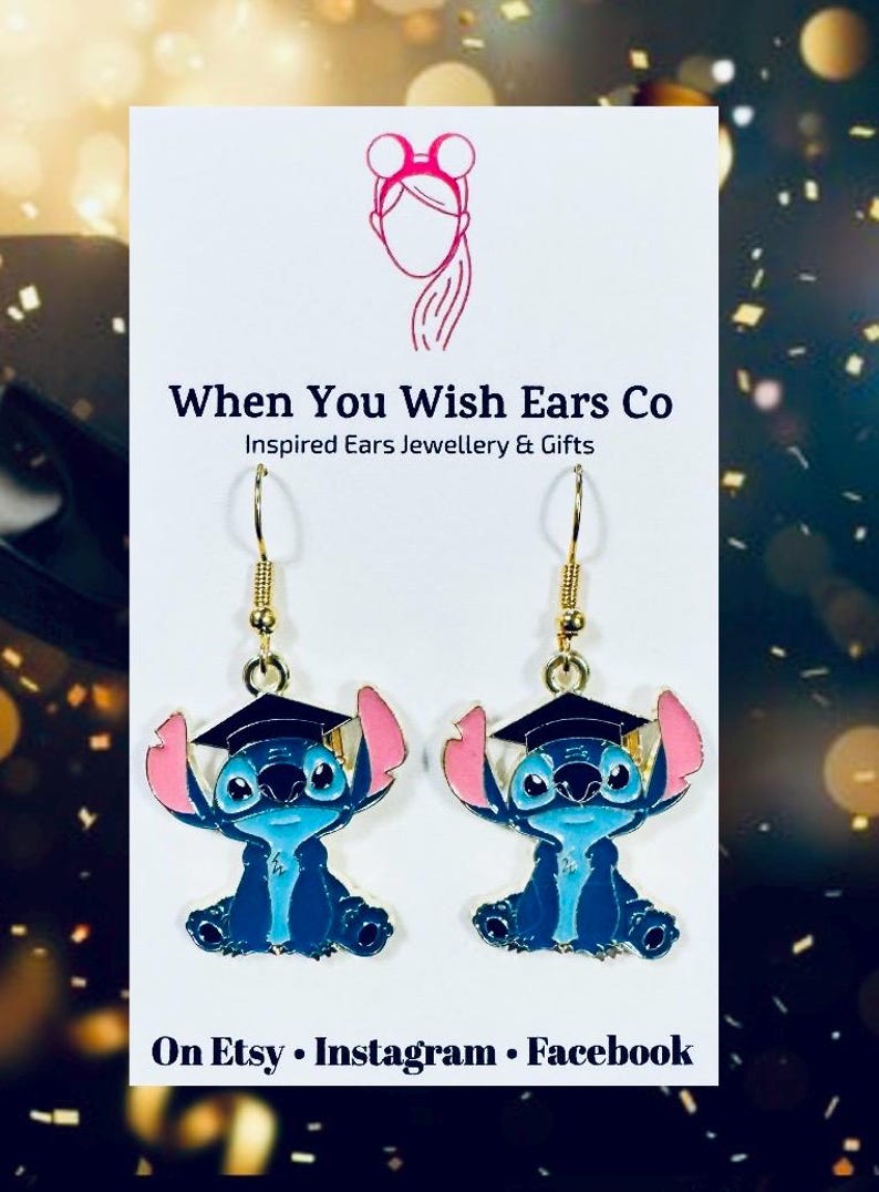 May include: Gold dangle earrings featuring a blue Stitch character wearing a graduation cap. The character has pink ears and a blue body. The earrings are on a white background with the text "When You Wish Ears Co Inspired Ears Jewellery & Gifts On Etsy Instagram Facebook".