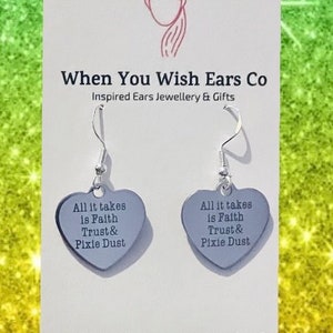 May include: Silver heart-shaped earrings with the text "All it takes is Faith Trust & Pixie Dust" on each earring. The earrings are on a white card with the text "When You Wish Ears Co Inspired Ears Jewellery & Gifts On Etsy Instagram Facebook".