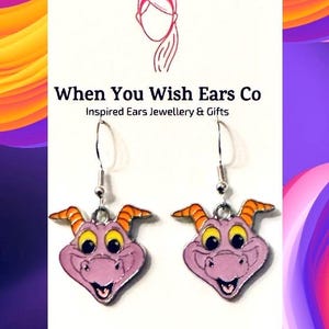 May include: Purple dragon character dangle earrings with orange horns and yellow eyes. The earrings are silver and have a hook closure. The earrings are on a white background with the text "When You Wish Ears Co Inspired Ears Jewellery & Gifts On Etsy Instagram Facebook".