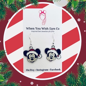 May include: A pair of silver dangle earrings featuring a cartoon Mickey Mouse wearing a Santa hat. The earrings are on a white card with the text "When You Wish Ears Co Inspired Ears Jewellery & Gifts On Etsy Instagram Facebook".